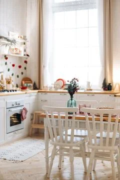 Cozy kitchen with a white dining table set with a green vase and red flowers Foto stock