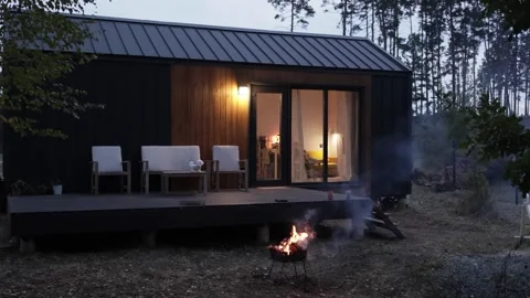 A Cozy Modern Cabin at Dusk, Complete with a Welcoming Fire Pit for Relaxation Stock Footage 308894056