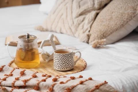 Cozy morning tea in bed with a teapot, mug, book, and decorative figurine on  Stock Photos