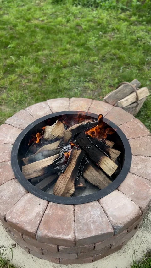 A Cozy Outdoor Fire Pit Featuring Flaming Logs Surrounded by a Lush Green Lawn Stock Footage 306076437
