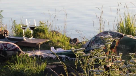 Cozy Picnic Setup by Lake with Campfire and Wine at Sunset Stock Footage 332307589