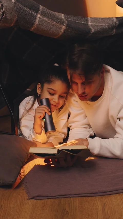 Cozy reading moment between father and daughter reading book under a blanket Stock Footage 316680459
