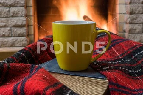 Cozy scene before fireplace with big green mug of tea, a book, and wool scarf Stock Photos