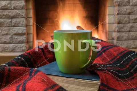 Cozy scene before fireplace with big green mug of tea, a book, and wool scarf Stock Photos