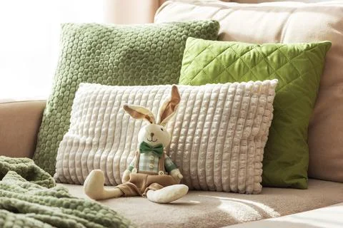 Cozy Sofa with Plush Easter Bunny Doll and Textured Pillows in Sunlight Stock Photos