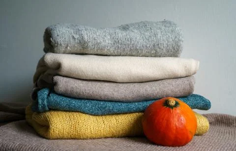 Cozy Stack of Folded Knitted Sweaters with Small Pumpkin in Warm Autumn Color Stock Photos