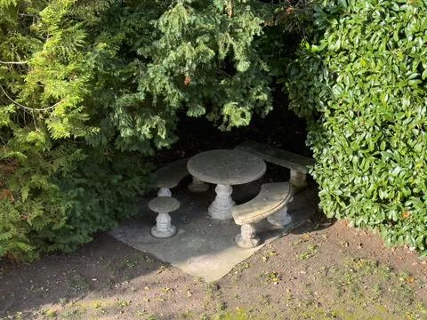 Cozy stone table set hidden among lush greenery in a peaceful garden corner.. Stock Photos