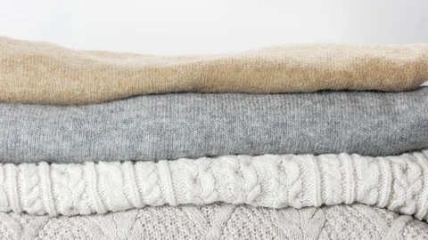 Cozy sweaters are lying in a pile. Woman hand touches them Stock Footage 126936219