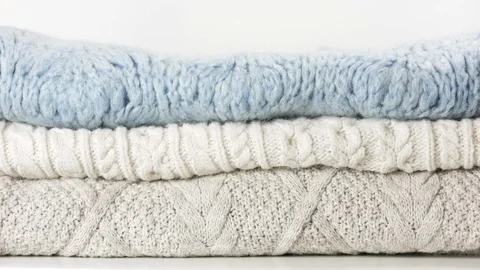 Cozy sweaters are lying in a pile. Woman hand touches them Stock-Footage 126936386