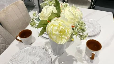 Cozy table setting with a white vase of artificial peonies and ceramic mugs.. Fotos Stock