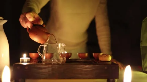 A cozy tea ceremony scene with warm candlelight, featuring a person preparing te Stock Footage 299386090