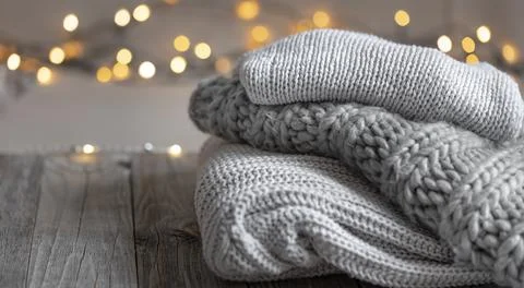 Cozy winter background with a stack of knitted sweaters and lights, copy space. Stock Photos