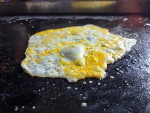Crack an egg onto a hot black flat pan.Prepare to cook. Top view. Stock Photos