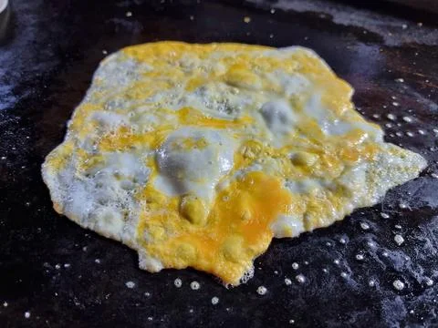 Crack an egg onto a hot black flat pan.Prepare to cook. Top view. Stock Photos