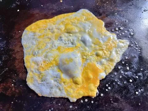 Crack an egg onto a hot black flat pan.Prepare to cook. Top view. Stock Photos