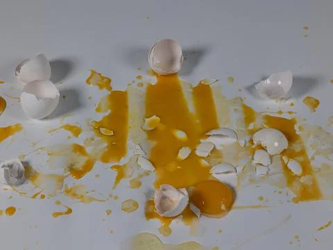 Cracked and broken eggs create messy scene on white background Foto stock