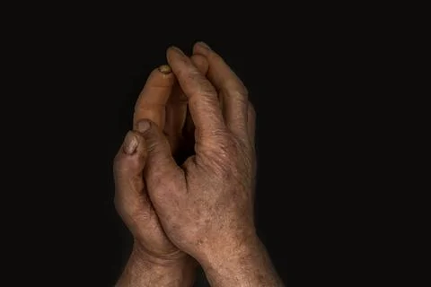 Cracked and ruined skin on overworked male pensionist hands praying on a blac Stock Photos