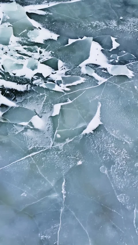 Cracked blue-grey ice sheet with jagged broken pieces and snow dust, showing Stock Footage 332096798