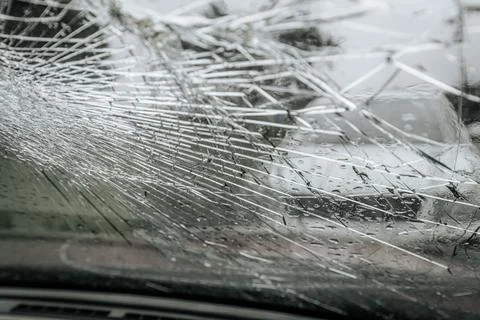 A cracked car windshield seen from the inside, with raindrops and a blurred Stock Photos