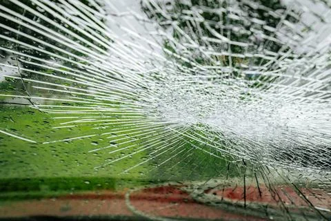 A cracked car windshield seen from the inside, with raindrops and a blurred Stock Photos
