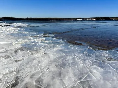 Cracked ice on a rocky shore of a thawed lake under a bright spring blue sky. Stock Photos