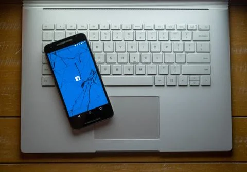 A cracked phone with the Facebook app loading sitting on a laptop Stock Photos