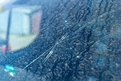 A cracked windshield shows damage caused by a stone or debris. The car is p.. Stock Photos