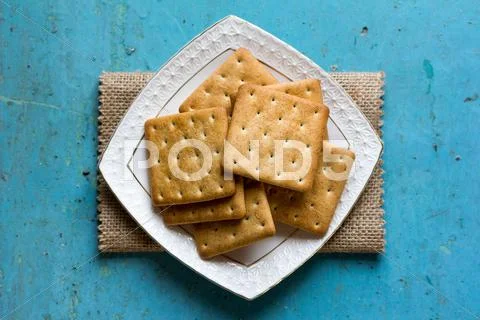 Cracker biscuits in a white ceramic square saucer on linen napkin Stock Photos