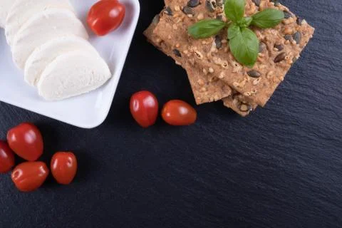 Crackers, mozzarella, tomatoes and basil on a black stone on a table Stock Photos