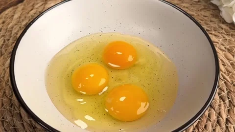 Cracking and whisking three fresh eggs in a white ceramic bowl for cooking Stock Footage 325071888