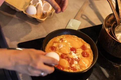Cracking egg into pan with tomatoes and yolk Stock Photos