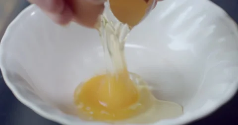 Cracking an egg into a white ceramic plate in preparation for cooking or mixing. Stock Footage 312283819