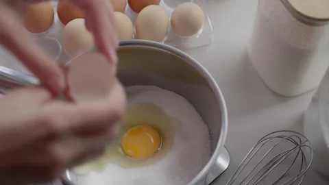 Cracking two eggs into sugar in saucepan, with egg tray, whisk and jars Stock Footage 339727336