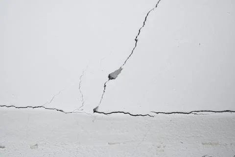 Cracks on the gray wall. Cement background. The concept of unfinished repairs. Stock Photos