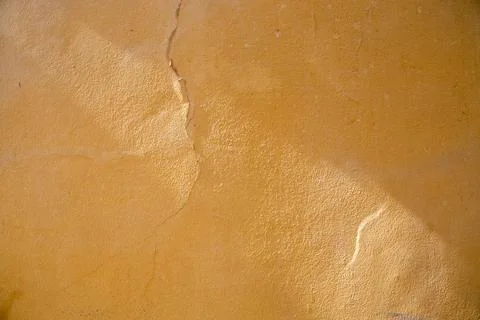 Cracks in the paint on the wavy uneven surface of a yellow bumpy Stockfoto's