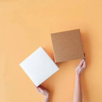 Craft boxes on an orange background with human hands. Place for text and lo.. Stock Photos