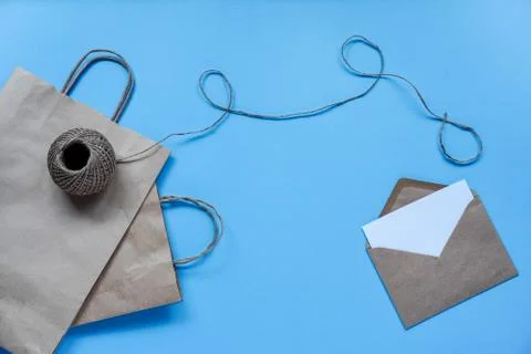 Craft paper bag with string and envelope with white sheet on blue background. Stock Photos