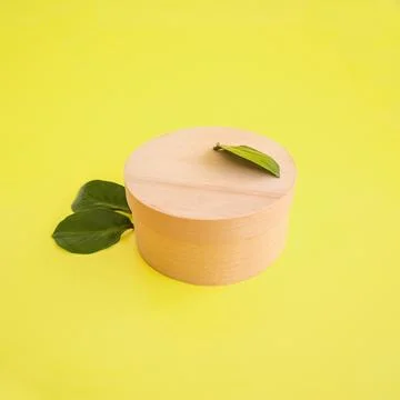 Craft round box on yellow background with green leaves. Place for text and .. Foto stock