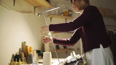 Craft woman pulling thread in knitting machine standing on table in workshop Stock Footage 87327374