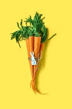 Craft wool thread carrots on yellow background. Minimalist decor for Easter.. Stock Photos