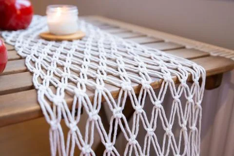 Crafted macrame runner lies, featuring detailed knotting and a burning candle Stock Photos