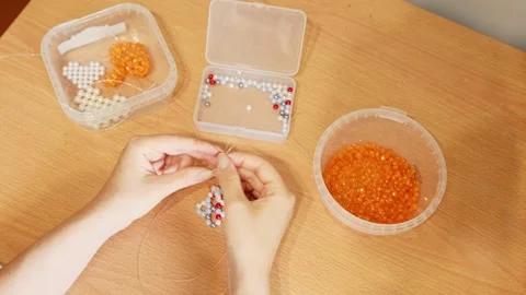 Crafting colorful beadwork hands threading small beads on wire at wooden ta.. Stock Footage 339568101