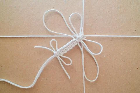 Crafting white macrame dragonfly knot on brown surface Stock Photos