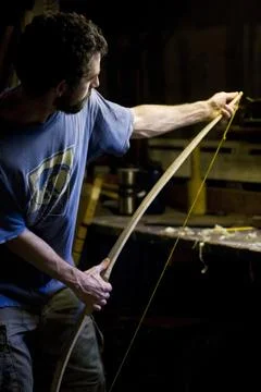 A craftsman attaches a string to one of his home-made bows in his home workshop Stock Photos