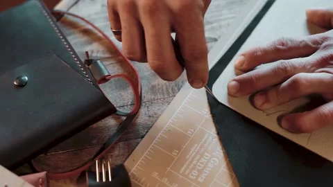 A craftsman cutting leather according to the pattern on wooden table in workshop Stockbeeldmateriaal 146244082