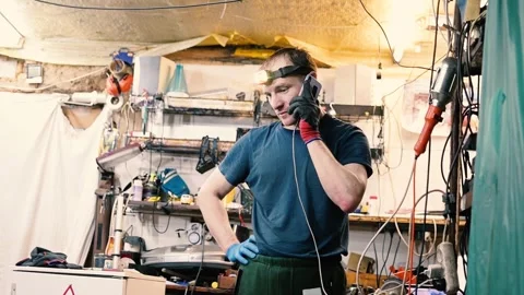 Craftsman with a Headlamp on his Head Talking on his Smartphone in a Workshop 動画素材 345043907