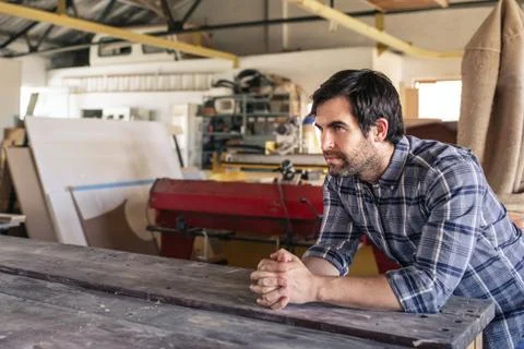 Craftsman leaning on a workshop bench deep in thought Foto stock