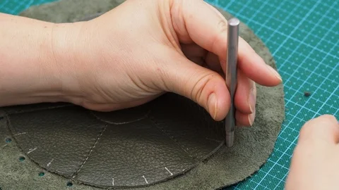Craftsman makes perforation in the stitched pouch by punch and hammer Stock Footage 97415499