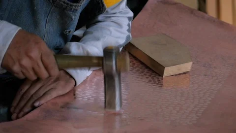 Craftsman pounding a sheet of copper with a hammer to give it texture Video stock 98843170