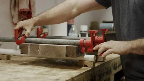A craftsman precisely adjusts pipe clamps, securing wood on a sturdy. Stock Photos